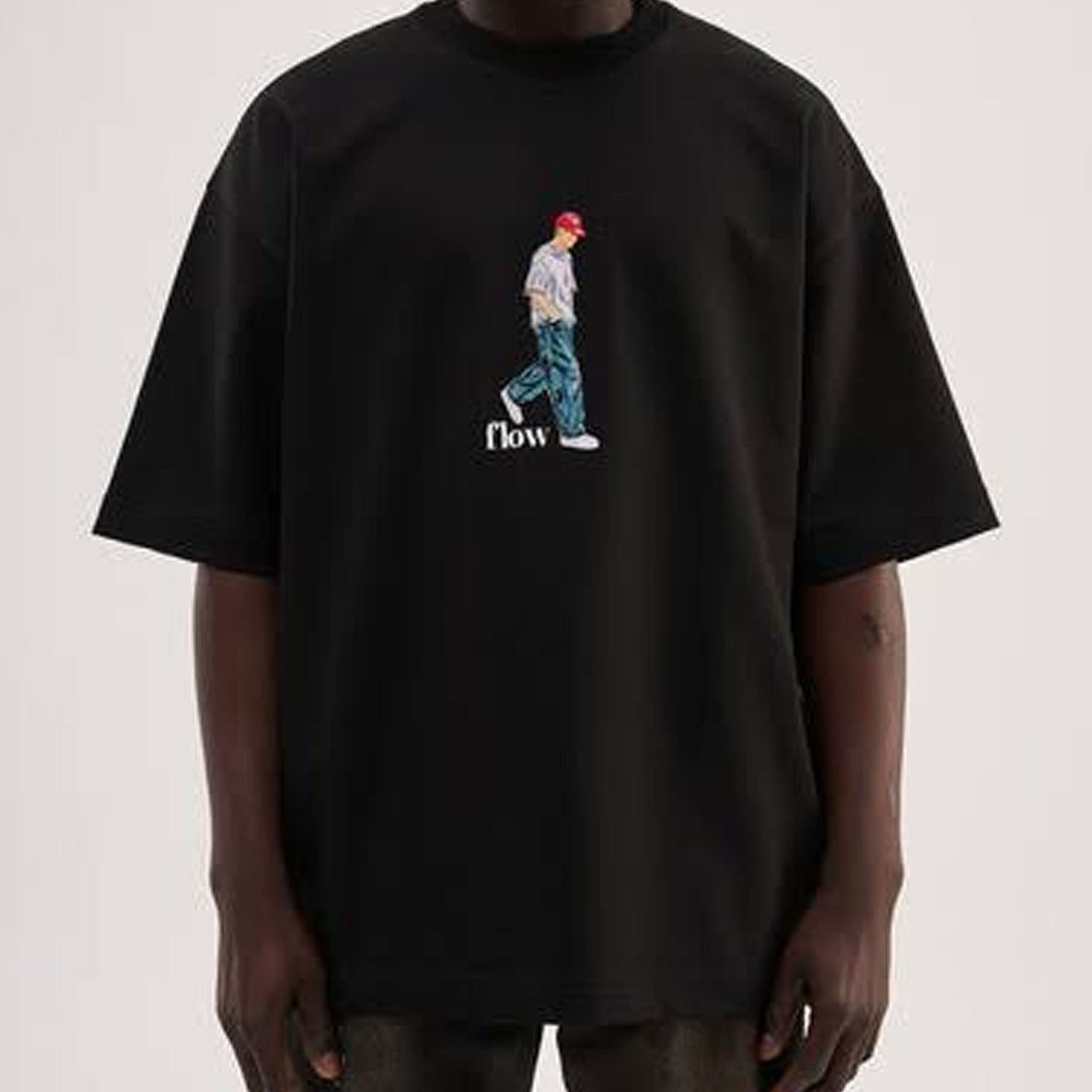 A person wearing an oversized black t-shirt with a central graphic of a walking figure in a red cap and blue pants, with the word 'now' printed below.