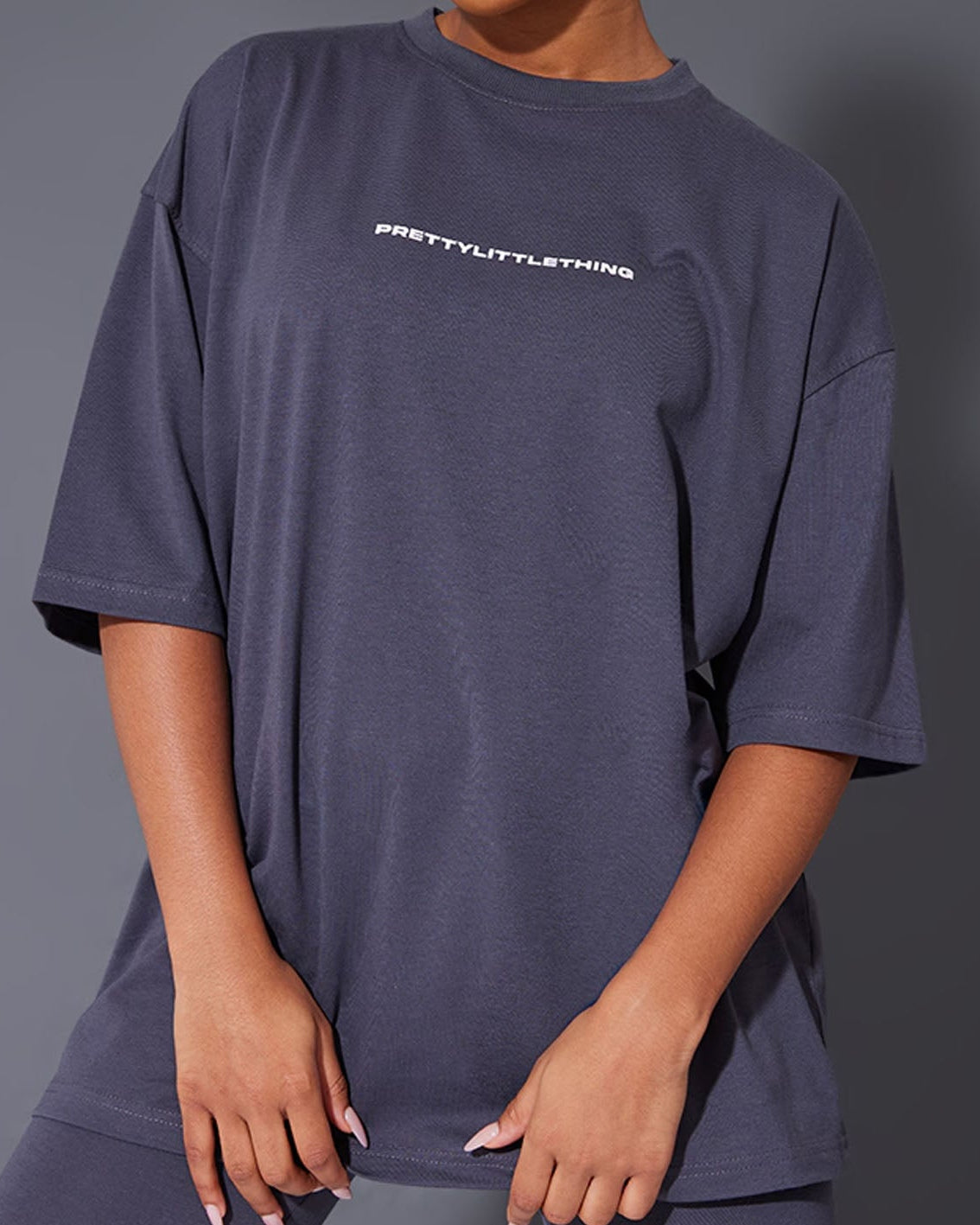 Person wearing a oversized t-shirt with 'PRETTYLITTLETHING' branding on a gray background