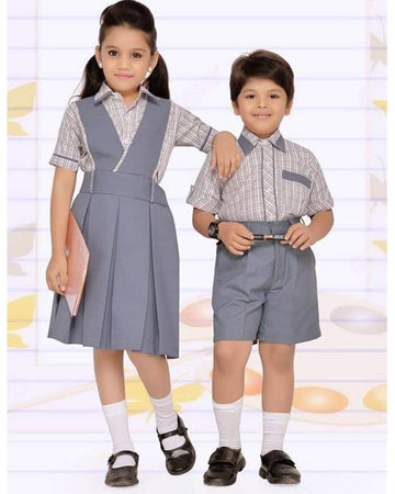 A girl and a boy modeling matching school uniform sets. The girl wears a gray pleated pinafore dress over a blue and white checkered short-sleeve shirt, paired with white socks and black shoes.