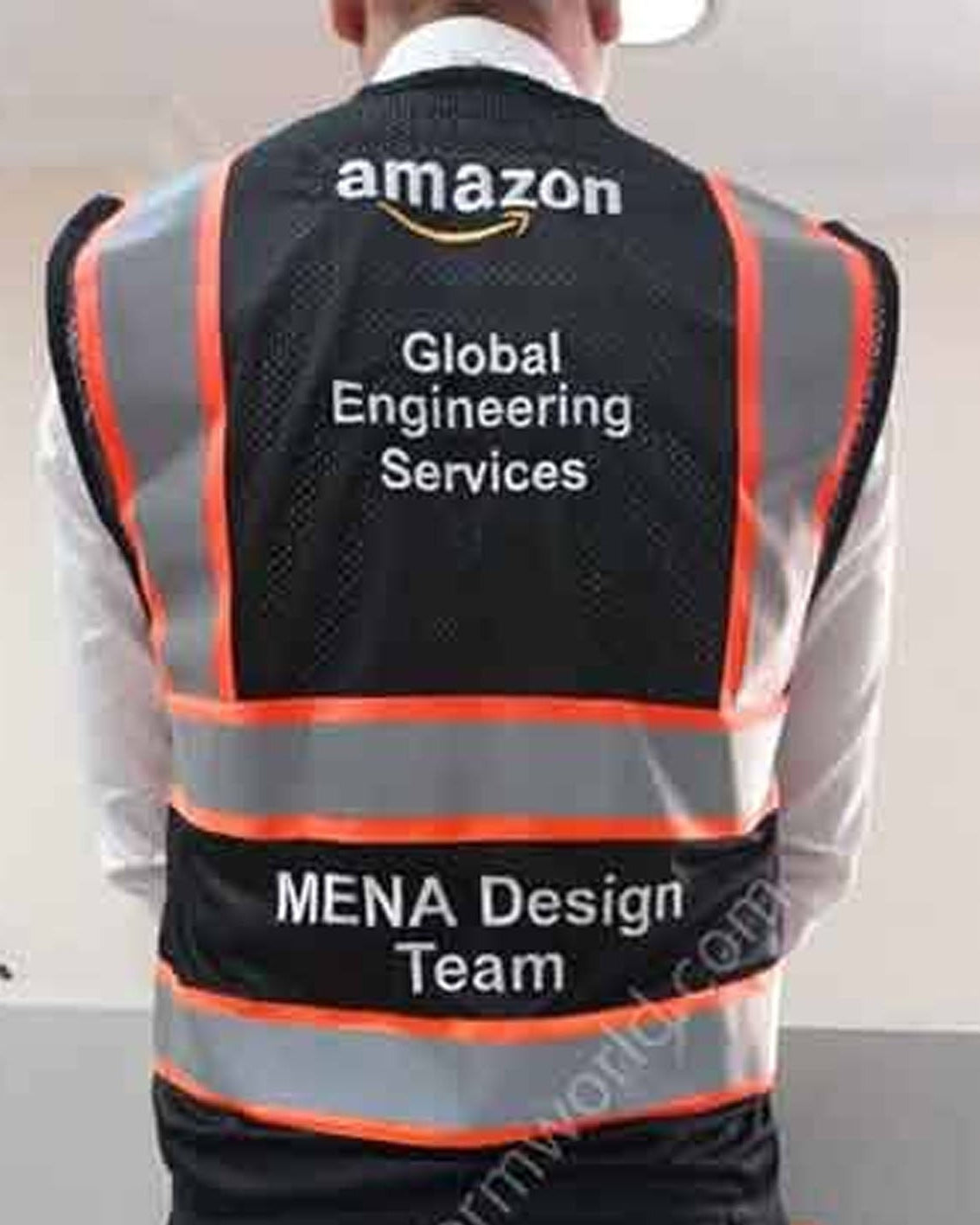 A person shown from behind wearing a black high-visibility safety vest with reflective silver stripes and orange trim. The vest has 'amazon' printed at the top, 'Global Engineering Services' in the center, and 'MENA Design Team' on a lower reflective band.