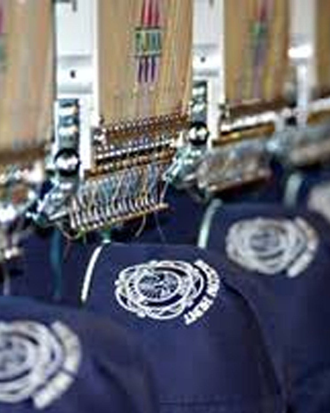 A close-up of navy blue fabric pieces with white embroidered circular logos, being processed by a row of industrial embroidery machines in the background.