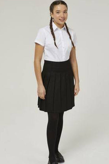 A girl modeling a school uniform consisting of a white short-sleeve button-up shirt, a black pleated skirt, black tights, and black shoes, standing against a light gray studio background.