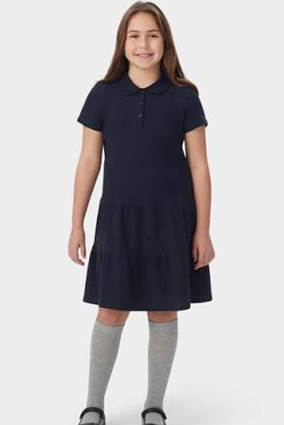 A young girl modeling a short-sleeve navy blue dress with a tiered skirt, paired with light gray knee-high socks and black shoes, against a light gray background.