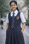 A young girl wearing a navy blue school uniform with a white shirt, striped tie, and a school crest on the chest, standing outdoors on a paved path.