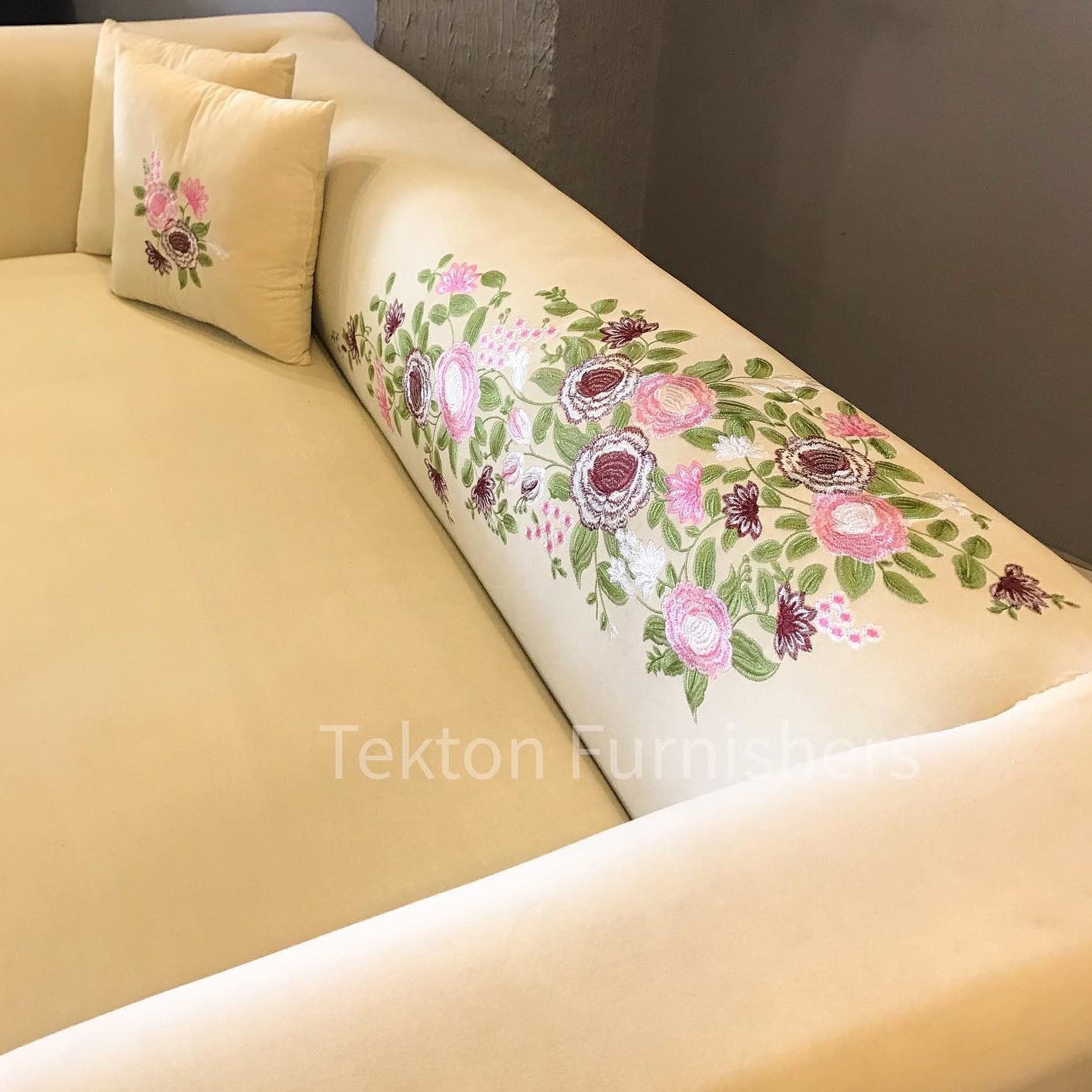 Beige sofa with floral patterned cushions and a decorative pillow against a plain wall.