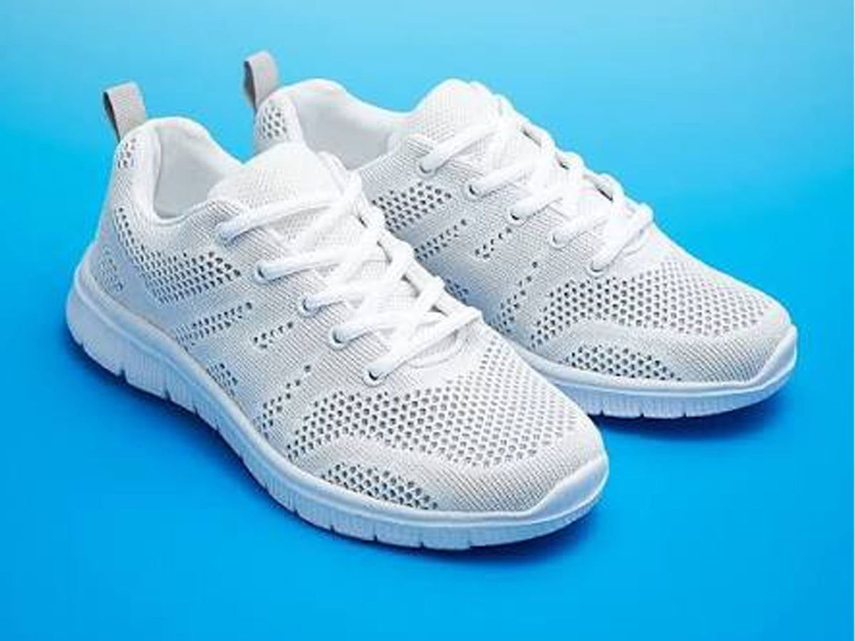 A pair of white knit athletic sneakers with white laces and white soles, displayed on a vibrant blue gradient background.
