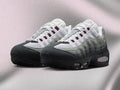 A pair of Nike Air Max 95 sneakers in a color gradient transitioning from white and light gray at the top to black at the toe and sole, displayed on a textured light gray background.