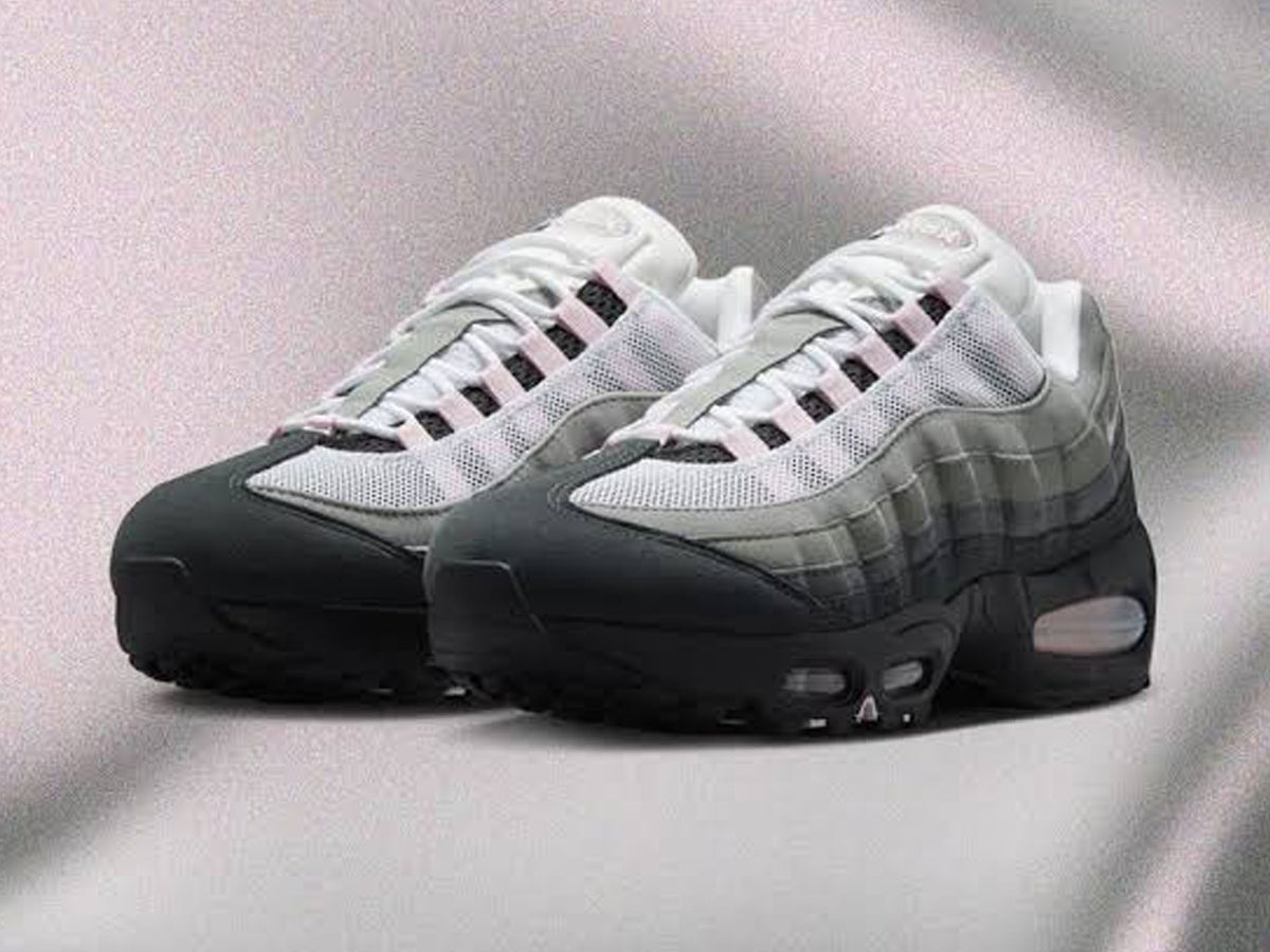 A pair of Nike Air Max 95 sneakers in a color gradient transitioning from white and light gray at the top to black at the toe and sole, displayed on a textured light gray background.