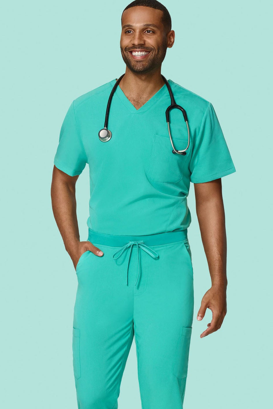 A man wearing a matching teal green medical scrub set with a V-neck top, drawstring pants, and a black stethoscope around his neck, standing against a solid light teal background.