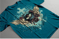 Blue t-shirt with a decorative design featuring an eye and floral elements on a gray surface.