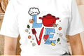 White t-shirt with colorful 'LOVE' graphic design featuring kitchen items.