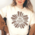 Person wearing a white t-shirt with a brown sunflower design and text.
