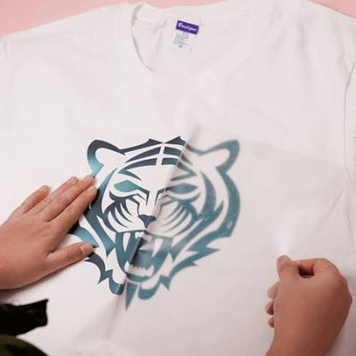 A white Gildan t-shirt with a blue and black tiger graphic, being held down by two hands to show the fabric's tear resistance.
