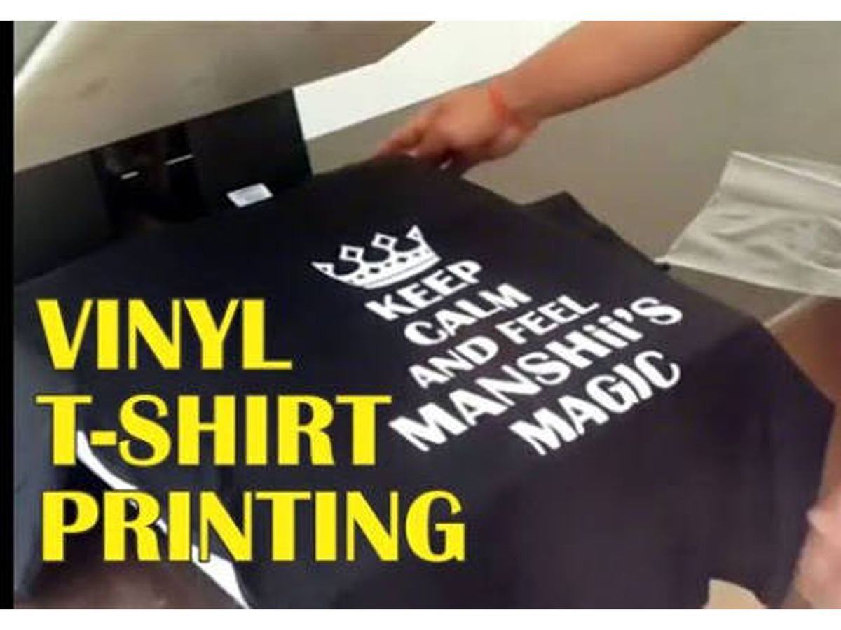 A black t-shirt with white printed text and a crown graphic is being held under a heat press, with large yellow text overlay reading 'VINYL T-SHIRT PRINTING'.