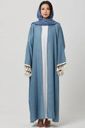 Woman wearing a blue abaya with white trim on a gray background