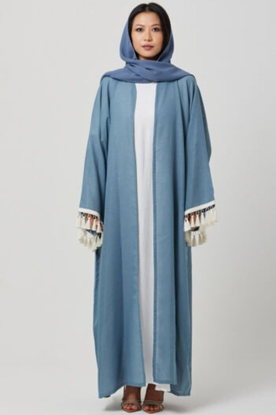 Woman wearing a blue abaya with white trim on a gray background