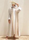Woman wearing a long, light-colored dress with a headscarf against a neutral background