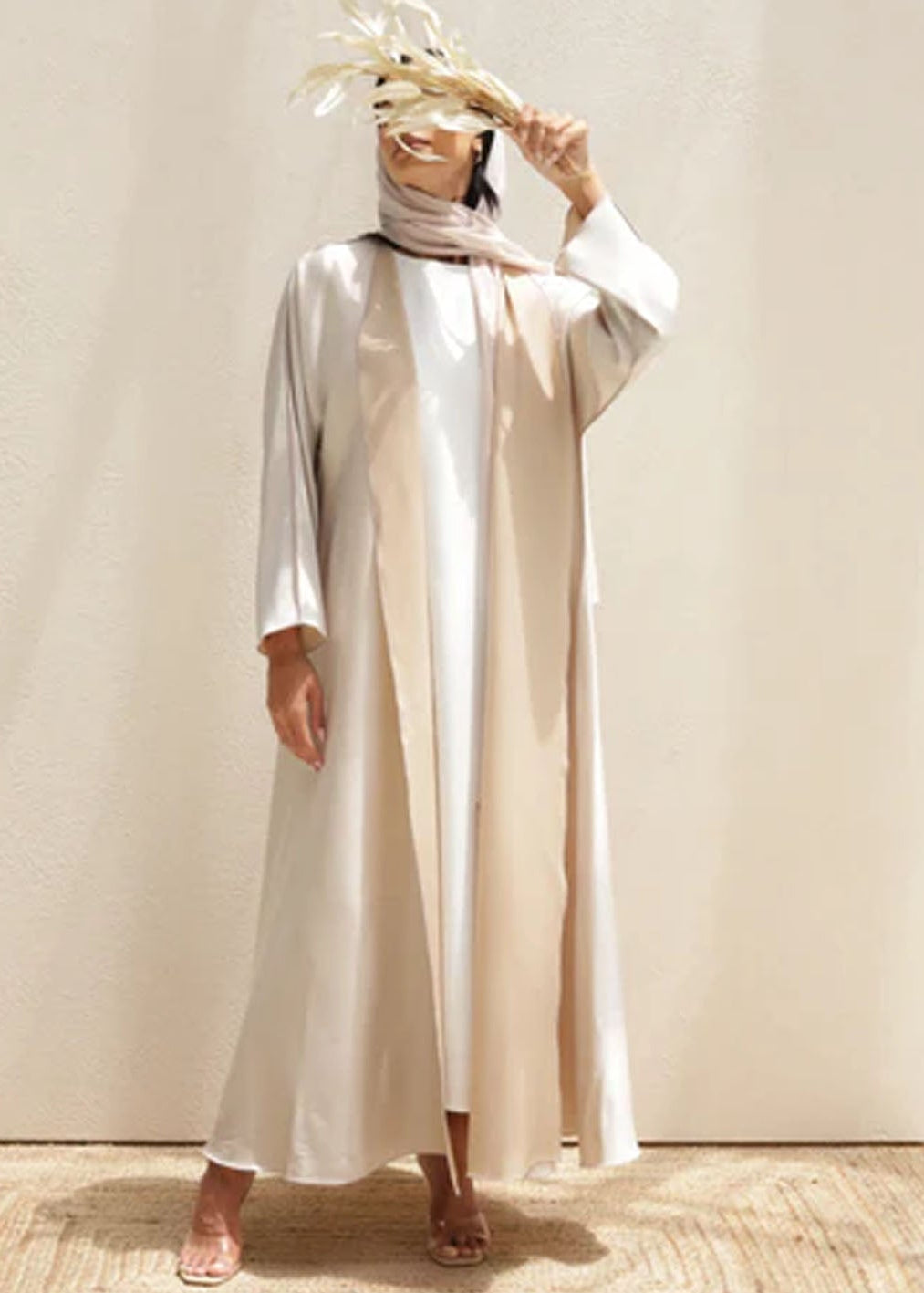 Woman wearing a long, light-colored dress with a headscarf against a neutral background