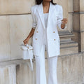 Person wearing a white suit with gold buttons against a stone wall.