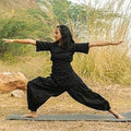 Person in black outfit practicing yoga outdoors with greenery in the background