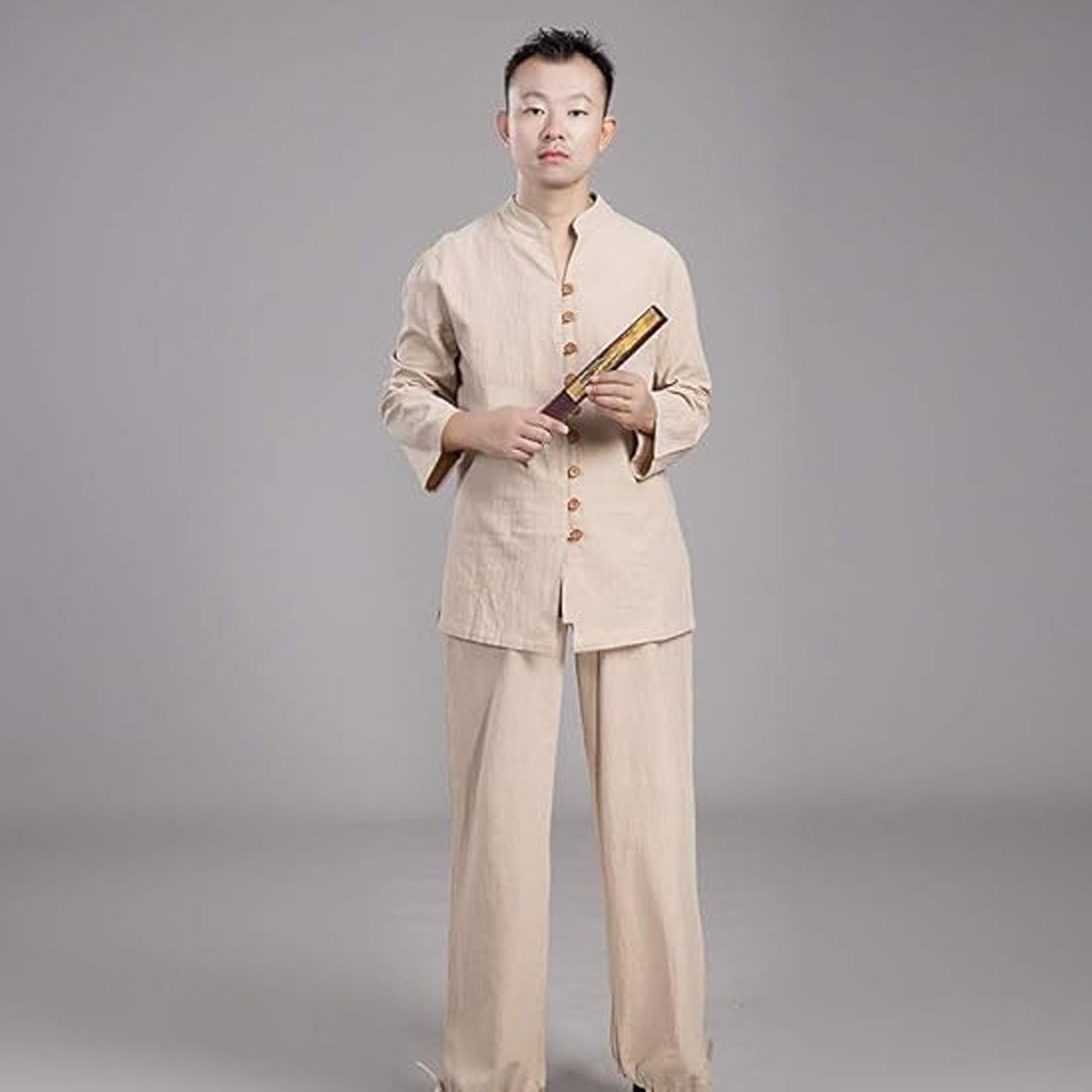 Person wearing a beige traditional outfit holding a book on a gray background