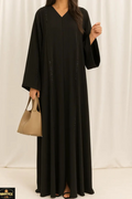 Woman wearing a black abaya holding a beige handbag against a white background