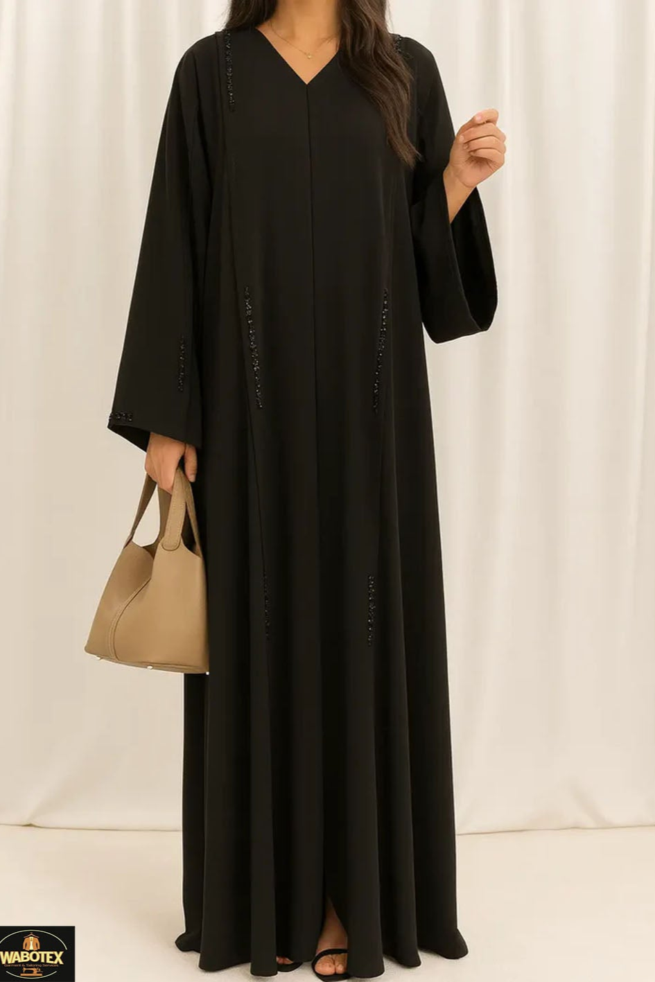 Woman wearing a black abaya holding a beige handbag against a white background