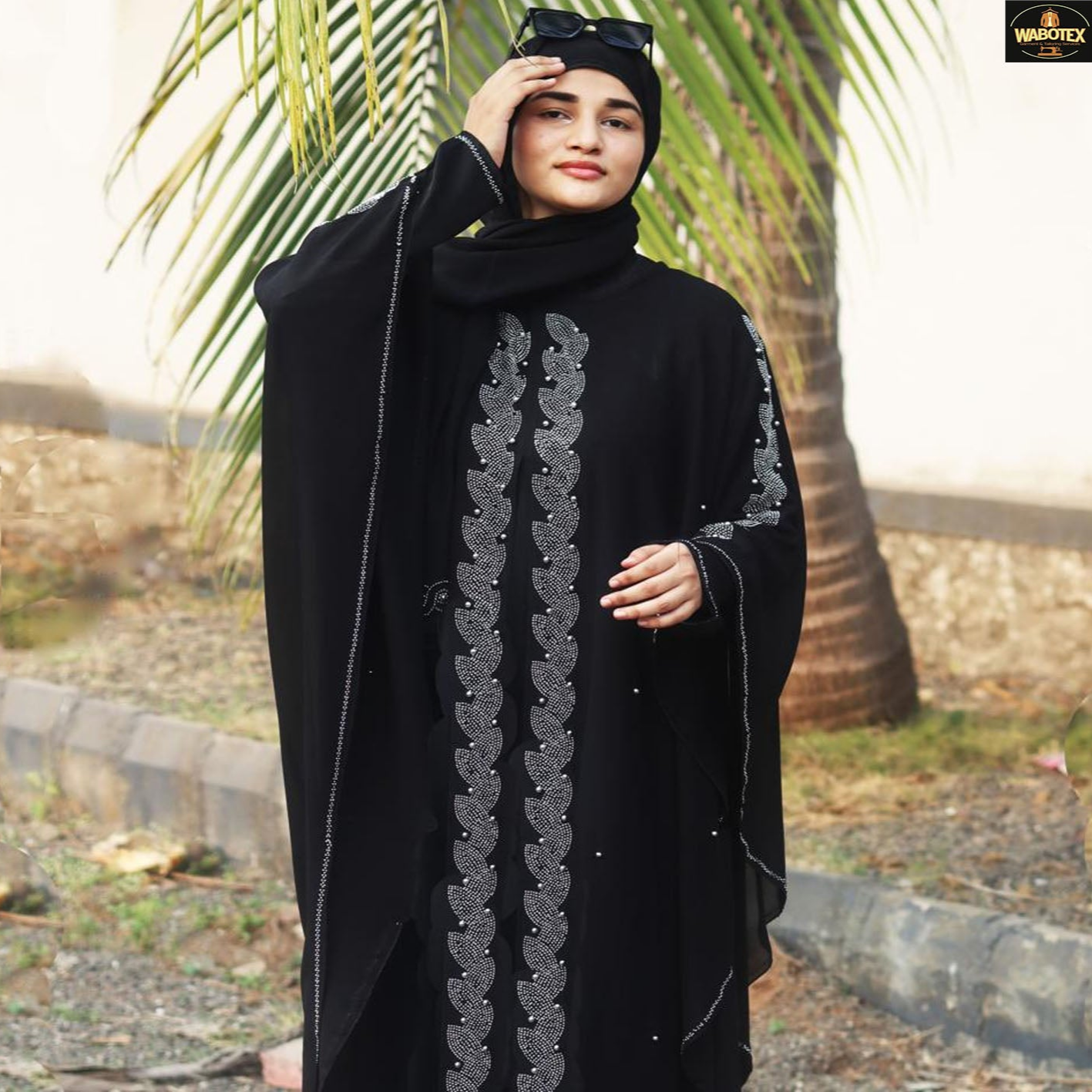 Woman wearing a black abaya with silver embroidery against a natural background