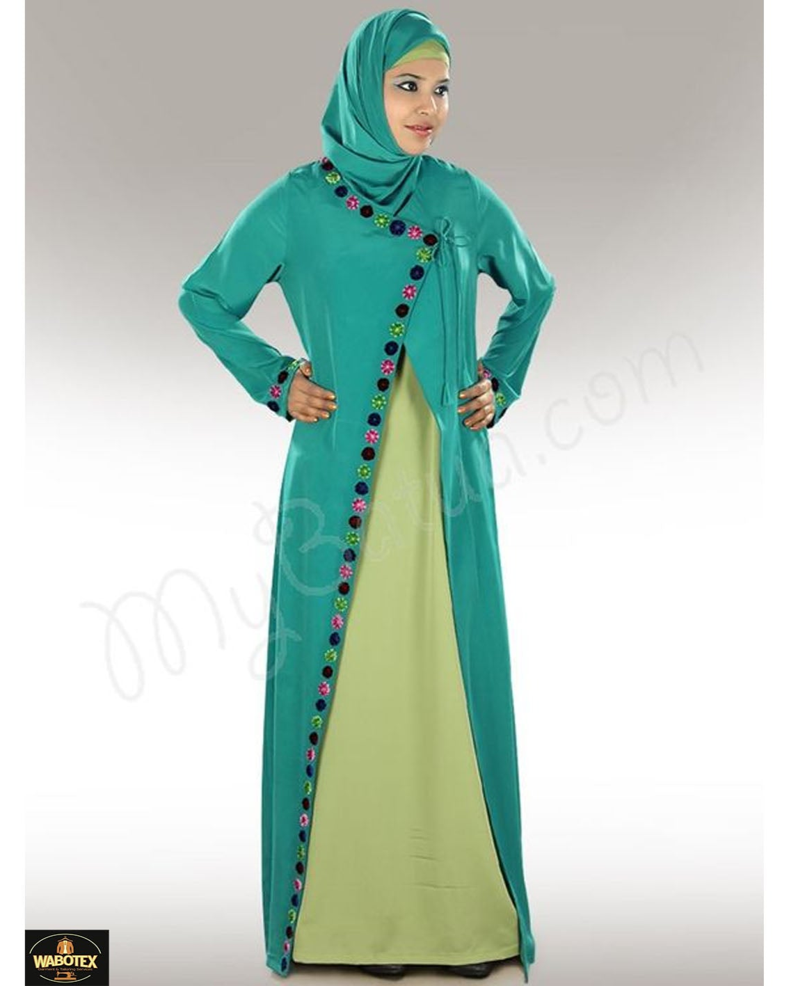 Woman wearing a teal and green dress with a hijab on a gray background