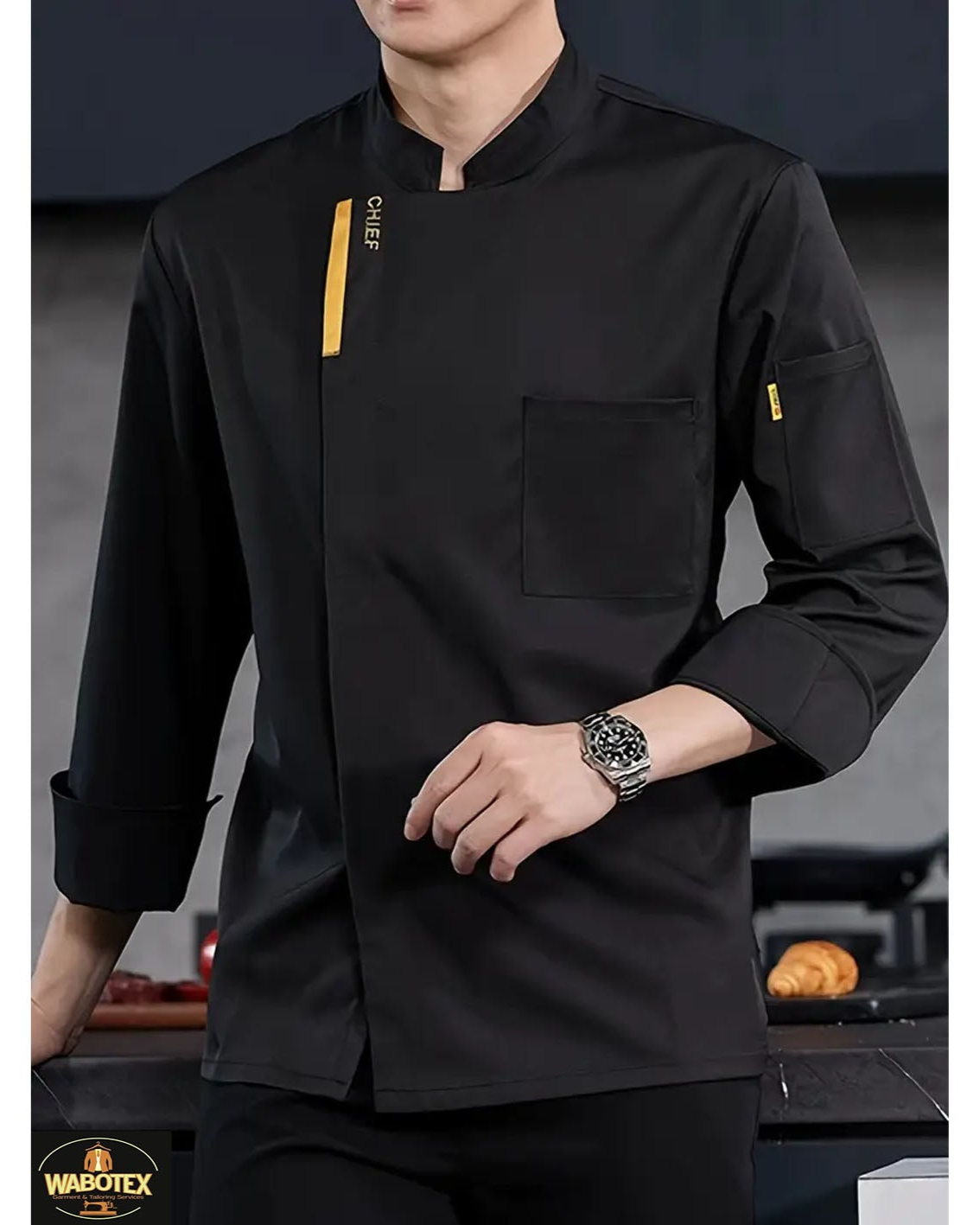 Black chef's jacket with yellow accents worn by a person, brand 'Wardtex' visible.