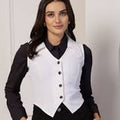 Woman wearing a white vest over a black shirt against a plain background