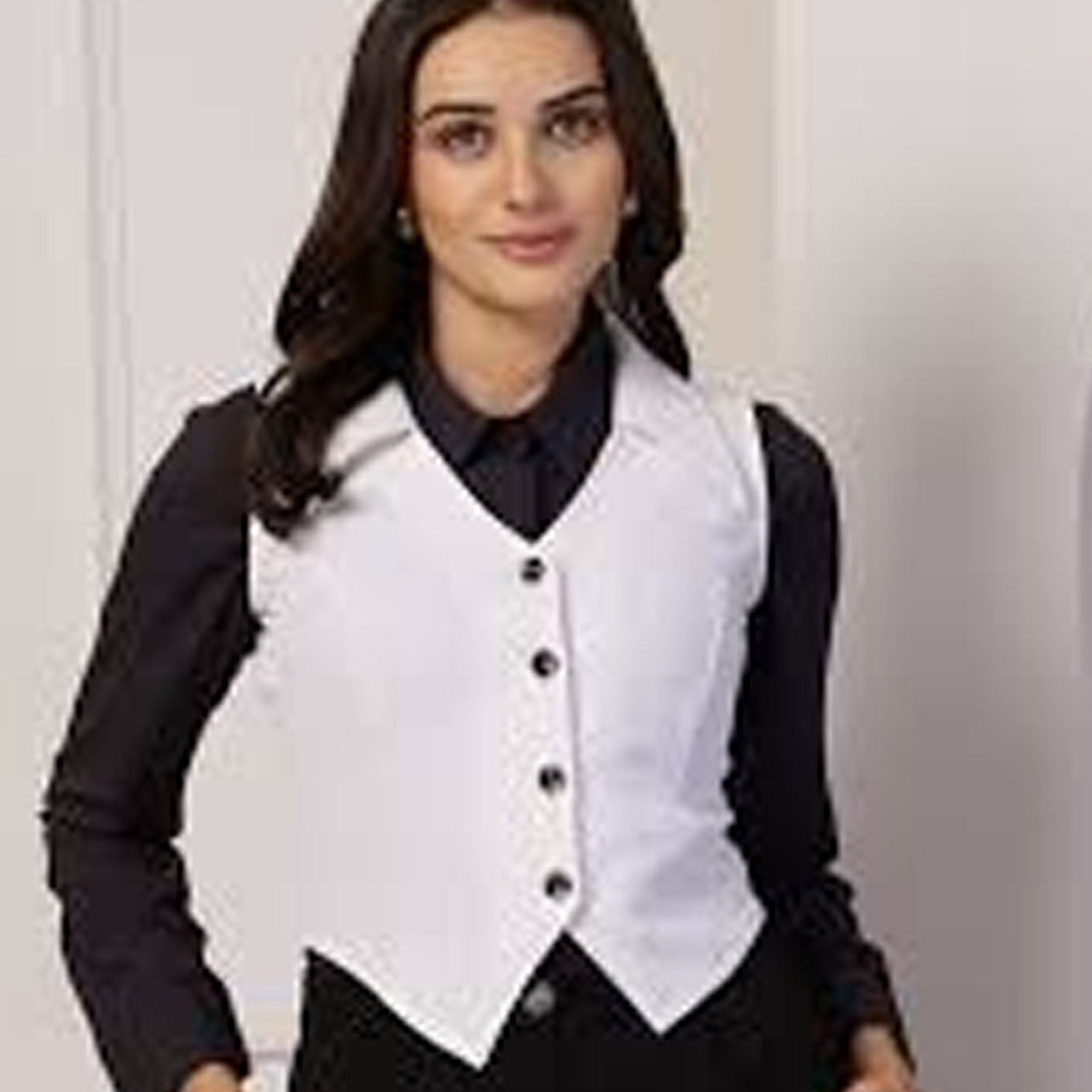Woman wearing a white vest over a black shirt against a plain background