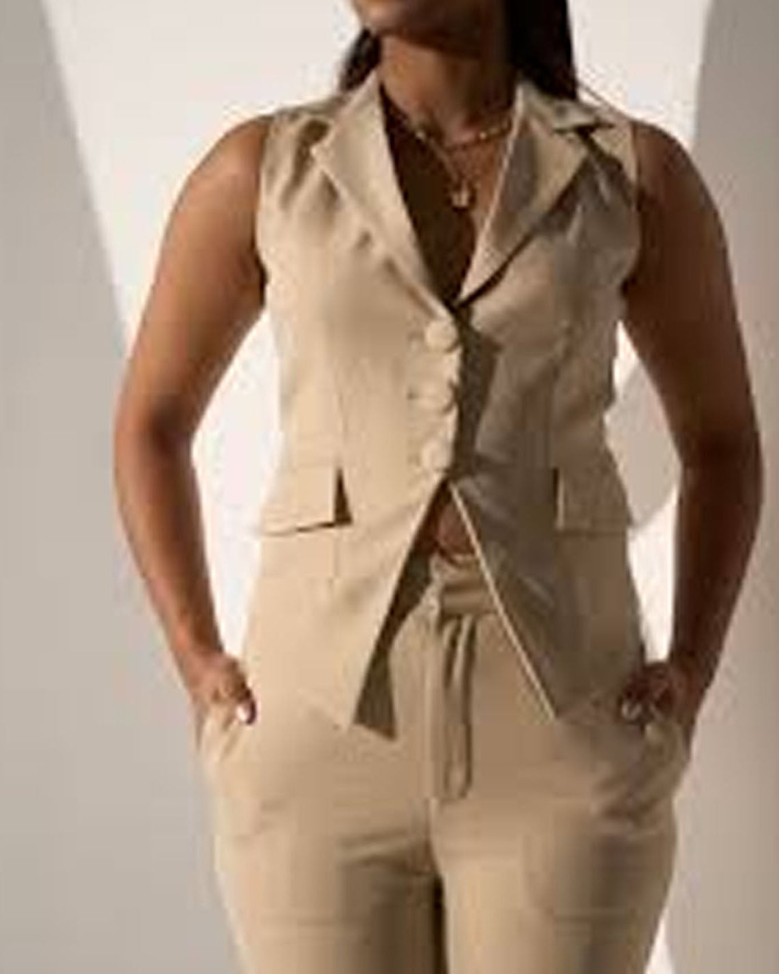 Person wearing a beige sleeveless jacket and pants set against a neutral background
