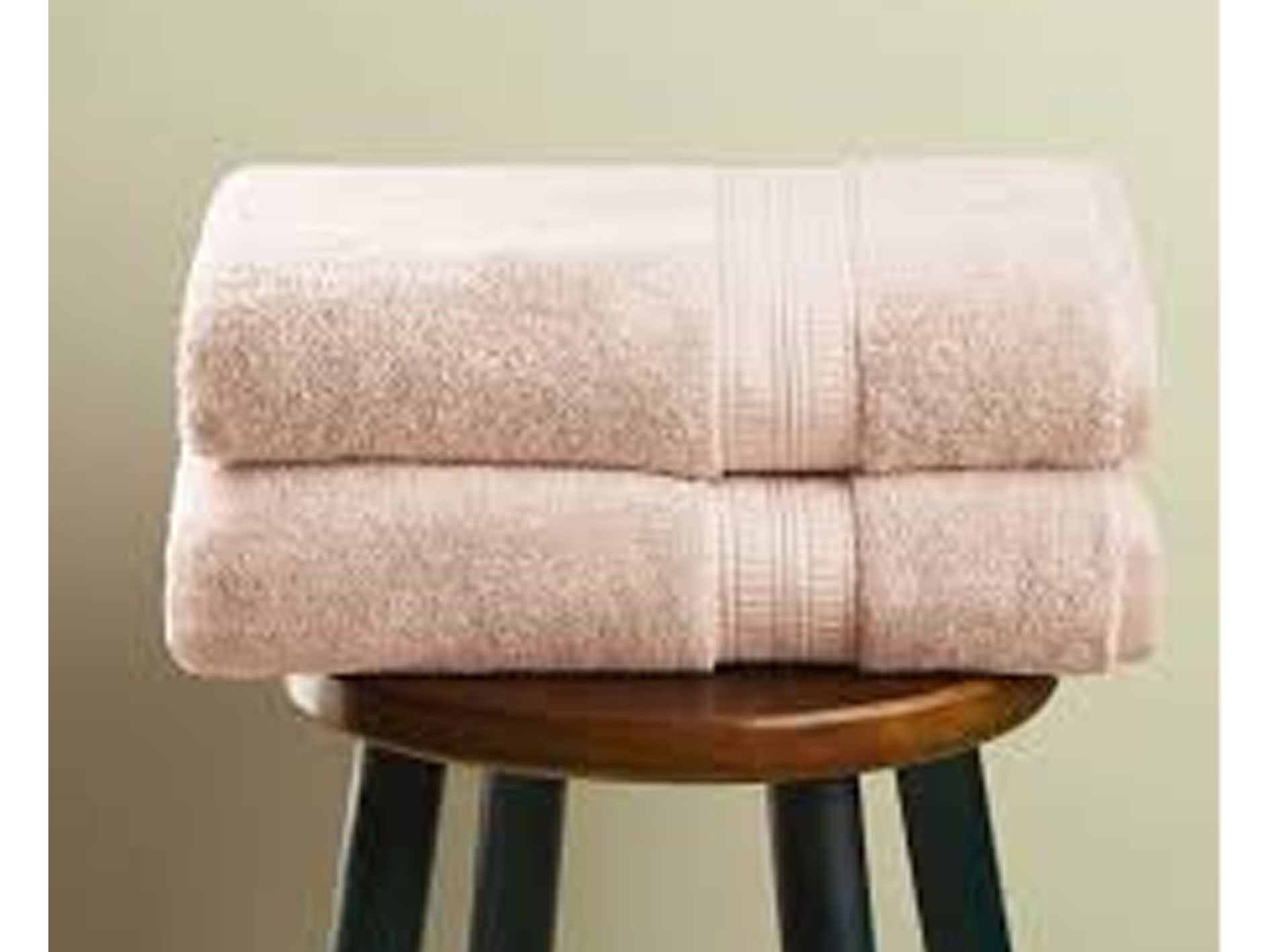 Stack of pink towels on a wooden stool against a green wall
