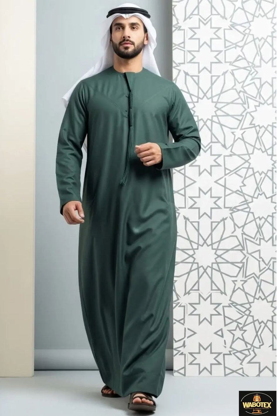 Man wearing a green traditional outfit standing against a white wall with geometric patterns.